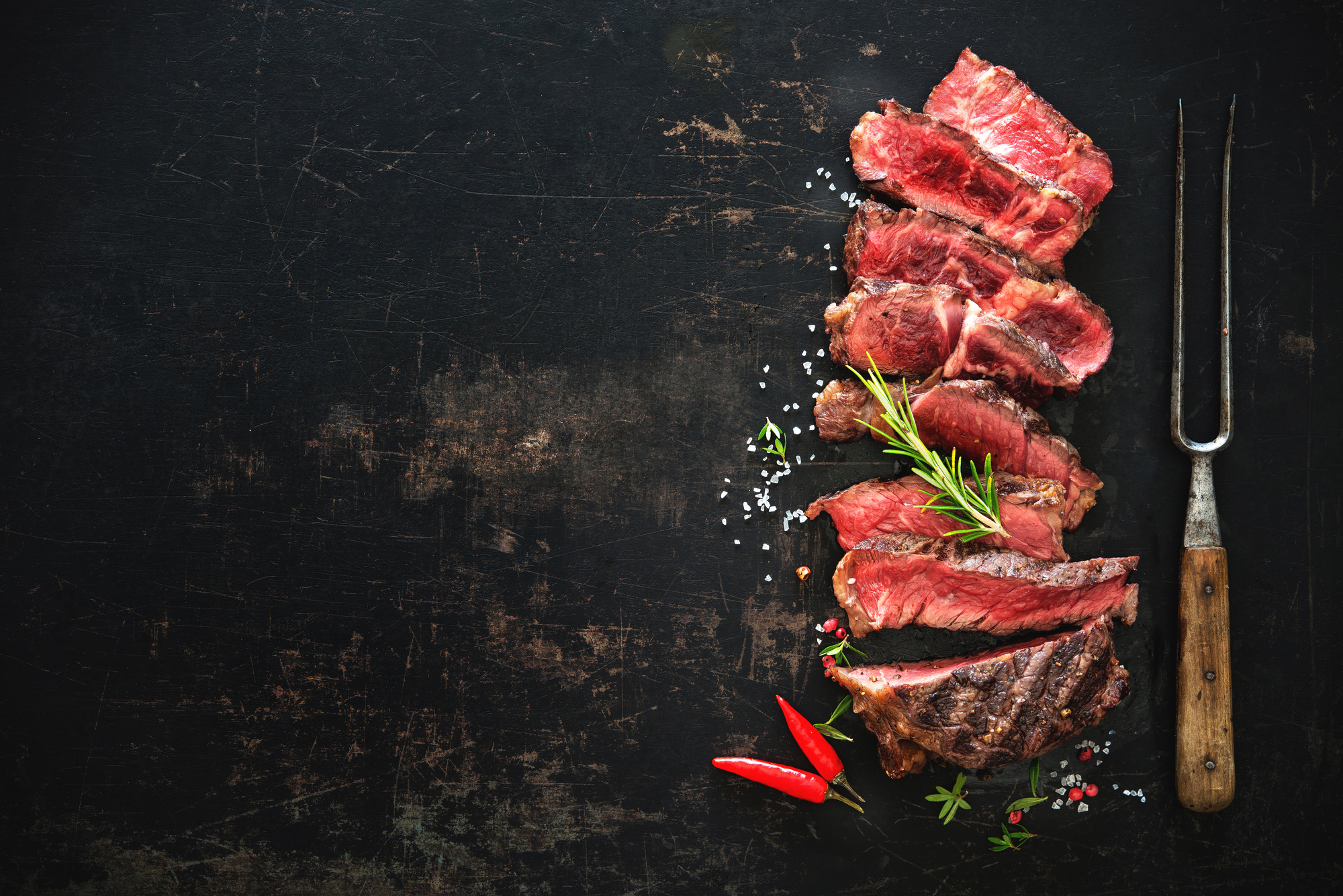 Sliced medium rare grilled beef ribeye steak on dark background