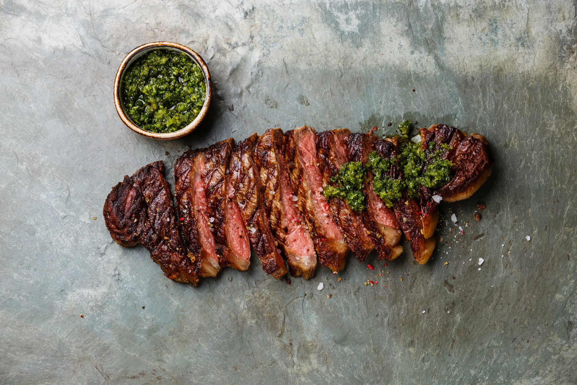 Sliced grilled beef barbecue Striploin steak with chimichurri sauce on gray stone slate background