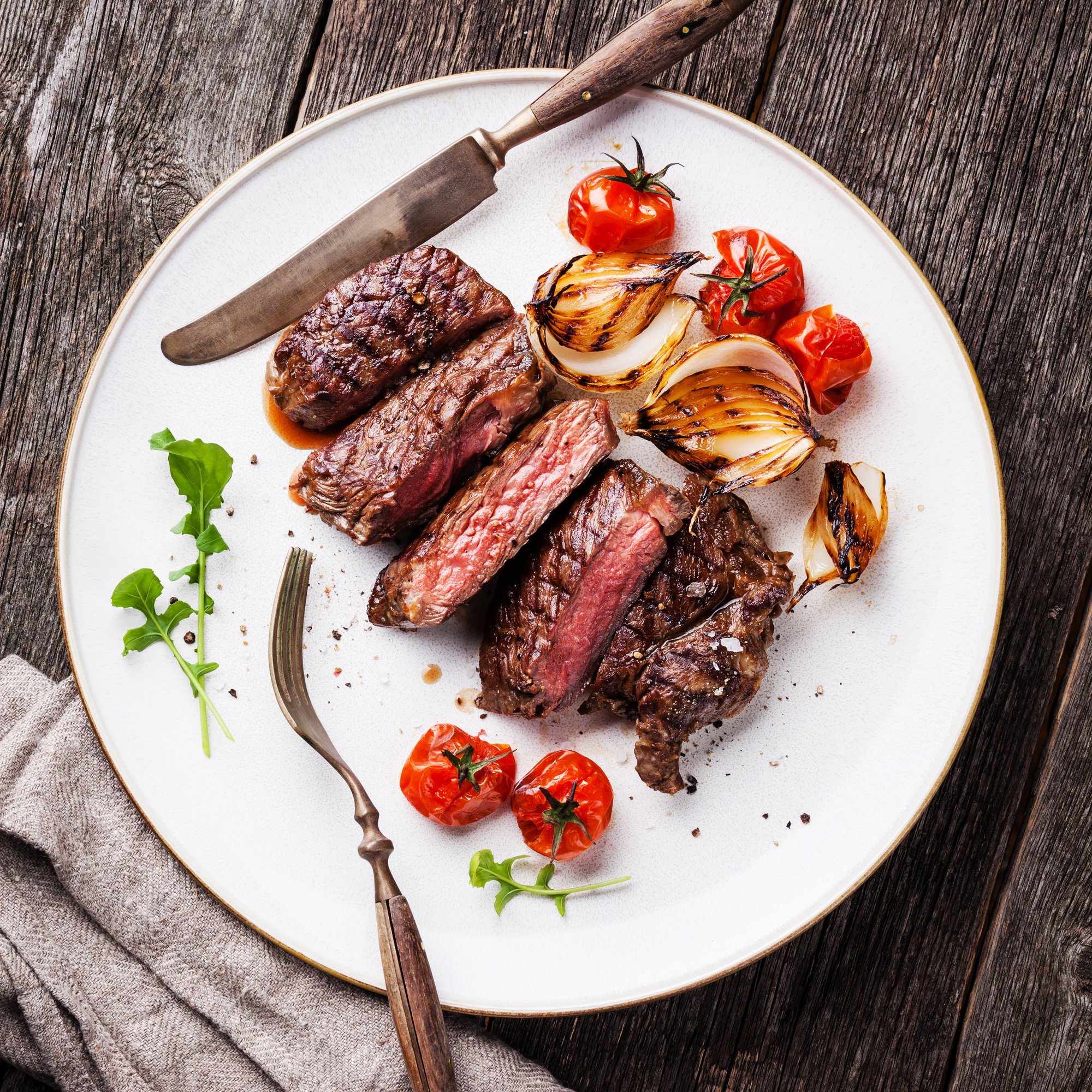 Sliced medium rare grilled Beef steak Ribeye with grilled onions and cherry tomatoes on plate on wooden background